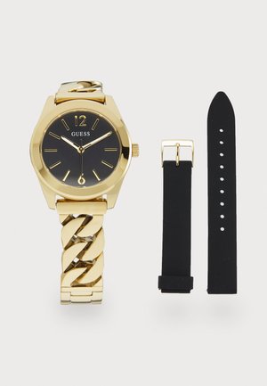 Montre Guess dorée avec un cadran noir, bracelet à maillons et deux bracelets interchangeables : un en caoutchouc noir et un noir avec boucle.