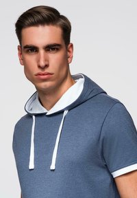 Modré tričko s kapucí a krátkými rukávy, bílé šňůrky a bílý akcent kolem výstřihu. Měkká tkanina s hladkým povrchem.