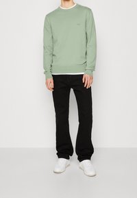 Mintgrön sweatshirt med rund hals och ribbad mudd, ihop med svarta jeans och vita sneakers. Enkelt, avslappnat outfit med logotypdetalj.