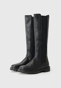 Bottes noires jusqu'aux genoux avec une finition en cuir texturé et une semelle en caoutchouc, dotées de panneaux latéraux élastiques pour un enfilage facile.