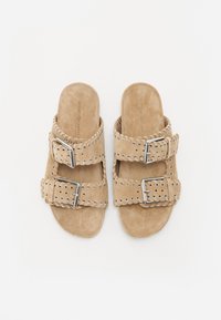Sandales en cuir suédé beige avec des sangles à double boucle, des découpes décoratives et des détails de couture. Semelle plate avec une texture lisse.
