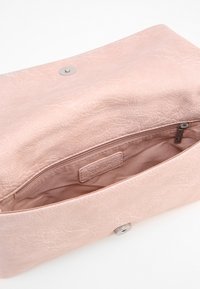 Pochette en cuir synthétique rose avec une surface texturée, une fermeture à pression à l'avant et une poche intérieure zippée pour le rangement.