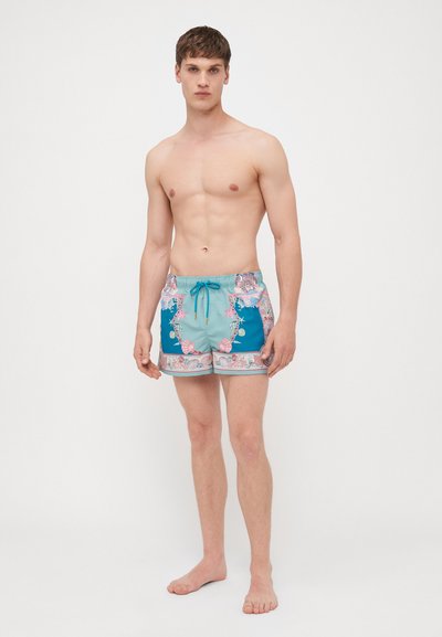 Μαγιό σορτς σε τιρκουάζ χρώμα με λουλουδάτα σχέδια σε ροζ και λευκό. Έχει ελαστική μέση με κορδόνι και πλαϊνές τσέπες. Υφασμάτινη υφή.