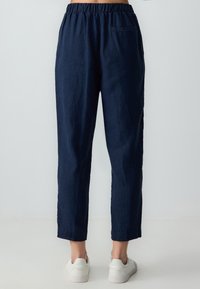 Pantalons en lin bleu marine avec une taille élastique, jambe fuselée et poche latérale, présentant une finition texturée et une coupe cropped.
