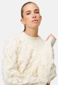 Kremfarvet sweater med tekstureret ribstrik, prydet med tredimensionelle blomsterapplikationer, med rund halsudskæring og tætsiddende manchetter.
