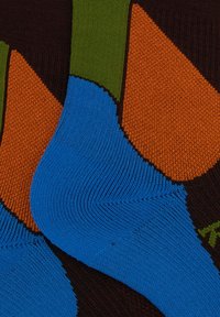Bunte Socken mit einer Mischung aus orange-, blau-, grün- und braunen Abschnitten. Der Stoff ist gestrickt und zeigt deutliche Farbblöcke und Texturen.