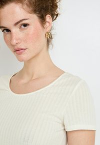 T-shirt à col rond en crème clair côtelé, avec des manches courtes, arborant une texture douce et des détails de couture subtils.