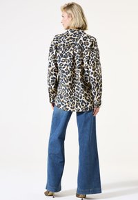 Een langemouwen shirt met luipaardprint in een relaxte pasvorm, gecombineerd met hooggewaisted wide-leg spijkerbroek; het heeft blauwe, beige en zwarte kleuren.