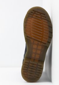 Podešev průhledně hnědé boty s tlustou, vzorovanou gumovou podrážkou na bílém pozadí se zaoblenými rohy.