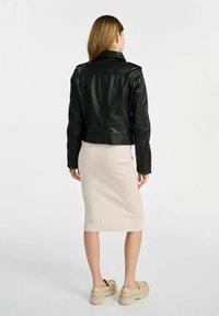 Czarna skórzana kurtka motocyklowa o dopasowanym kroju. Zauważalne pagony na ramionach i zamki błyskawiczne na rękawach. Nosi ją się na prążkowanej, beżowej spódnicy sięgającej do kolan.