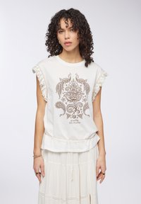 Top senza maniche color crema con frange, caratterizzato da una stampa marrone a paisley e floreale, con la scritta "Go With the Flow" al centro.