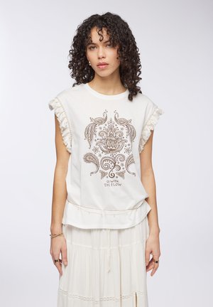 Top senza maniche color crema con frange, caratterizzato da una stampa marrone a paisley e floreale, con la scritta "Go With the Flow" al centro.