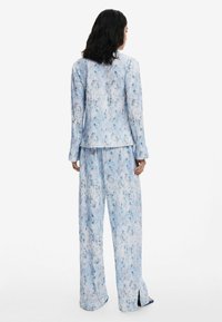 Un costume à imprimé floral bleu comprenant une veste ajustée et un pantalon à jambes larges, fabriqué en tissu doux, avec des manches longues et des fentes sur les côtés du pantalon.