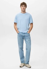 Světle modré tričko s krátkým rukávem a kulatým výstřihem, doplněné světle modrými džíny s rovnými nohavicemi a béžovými teniskami. Pohodlný a ležérní styl.