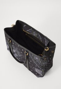 Zwarte canvas draagtas met een paisley patroon in wit en groen. Gouden hardware, dubbele zwarte handgrepen en een ritsvak binnenin.