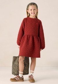 Rode, gewatteerde jurk met een ronde halslijn, pofmouwen en een uitlopende rok; gecombineerd met een tas met luipaardprint en gedessineerde schoenen.