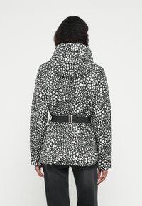 Μπουφάν πάπλωμα με μαύρο και άσπρο ζωικό σχέδιο, με κουκούλα και ζώνη στη μέση. Υφασμάτινη υφή με έντονη λεπτομέρεια μοτίβου.