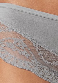 Grijze lingerie van een gladde stof met delicate bloemenkant langs de rand, die ingewikkelde patronen en texturen benadrukt.