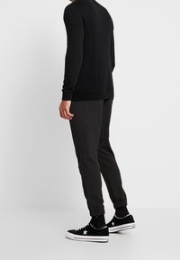 Mustapaitainen pitkähihainen villapaita yhdistettynä tummanharmaisiin kapeaan nilkkahousuihin ja mustiin lenkkareihin, joissa on valkoinen tähetunnus sivussa.