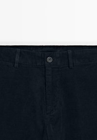 Pantalons en velours côtelé bleu marine avec une surface texturée, fermeture à bouton à l'avant et passants de ceinture. Détail de poche gauche visible.