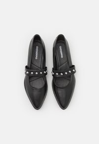 Zapatos de cuero negro con punteras afiladas, que cuentan con una amplia correa decorada con tachuelas plateadas en el mediopié. Forro interior suave.