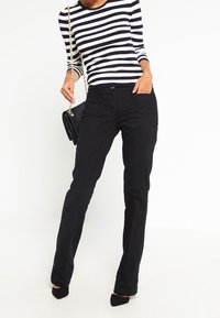Zwarte rechte broek met een gladde textuur, gedragen met een marineblauw en wit gestreept shirt. Accessoires omvatten een handtas met kettinghengsel.