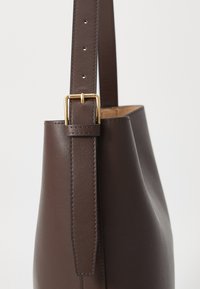 Borsa a spalla in pelle marrone con una texture liscia, dotata di una fibbia in metallo dorato e di una tracolla regolabile. Design semplice e affusolato.