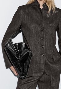 Costume texturé gris foncé avec col mandarin, doté de cinq boutons. Sac à main en cuir noir avec un motif en relief façon crocodile.