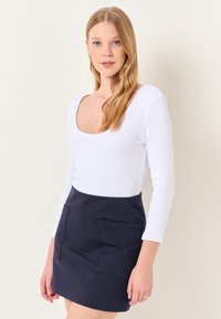 Biała, prążkowana bluzka z długim rękawem i kwadratowym dekoltem, zestawiona z granatową mini spódnicą z dwoma przednimi kieszeniami. Gładka tekstura, dopasowany krój.
