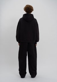 Sudadera negra extragrande con capucha, mangas largas y hombros caídos, combinada con pantalones negros sueltos. Textura suave en toda la prenda.