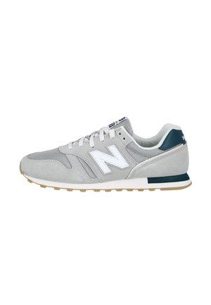 Zapatilla New Balance gris y blanca con empeine de ante y malla, cordones blancos, suela de goma y detalle en el talón azul oscuro, vista lateral.
