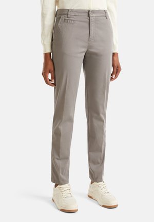 Osoba ubrana w proste szare spodnie, białe sneakersy i kremowy długi rękaw, stojąca na jednolitym tle.