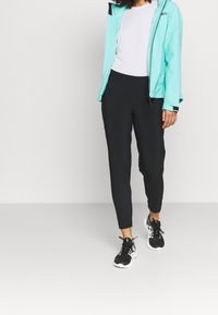 Ljusblått vattentätt jacka, vit topp, svarta tapered byxor och svarta sportskor med vita accenter. Lämplig för utomhusaktiviteter.