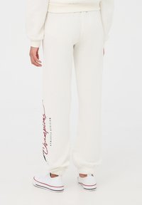 Białe, miękkie dresy z elastycznymi mankietami. Z boku znajduje się nadruk w kolorze czerwonym z napisem "Mistrzowska Dywizja Atletyczna". Prosty krój, luźny fason.