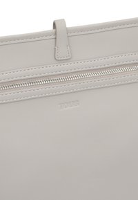 Gray leather bag featuring a zip closure, subtle stitching details, and a debossed "TOUS" logo on the front. Smooth texture overall.