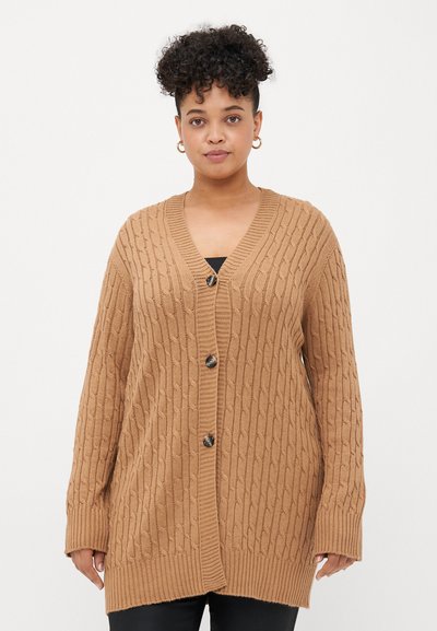 Cardigan long en maille torsadée beige, avec un col en V, une fermeture par boutons, et des poignets et un ourlet côtelés. Texture douce et coupe décontractée.