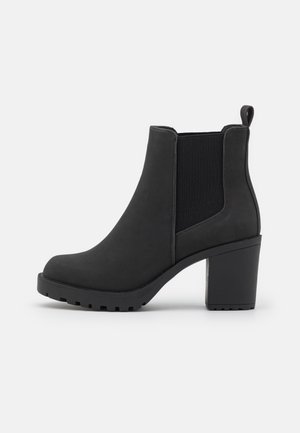 Czarny botek na kostkę z masywnym obcasem, elastyczną boczną wstawką i pętelką do ściągania, prezentowany na białym tle.