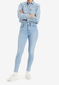 Jeans ajustados de tiro alto de mezclilla azul claro con una textura suave, que cuentan con un cierre de botón y diseño de cinco bolsillos, combinados con una camisa de mezclilla a juego.