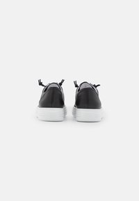 Black leather sneakers with white rubber soles, featuring two black pull tabs at the back and a simple design, no visible patterns.