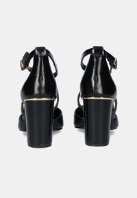 Sandalias negras de tacón alto con un acabado de cuero brillante, parte trasera cerrada, tira en el tobillo, acento dorado cerca del tacón y un diseño de tacón grueso y resistente.