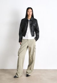 Zwarte lederen cropped jack met knoopsluiting, gecombineerd met een wit shirt en beige cargo broek met ritsen en zakken. Zwart hoge hakken.