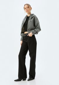Sudadera gris corta con cremallera, camiseta negra ajustada y pantalones negros a rayas. Combinados con zapatos de tacón negros y un cinturón ancho.
