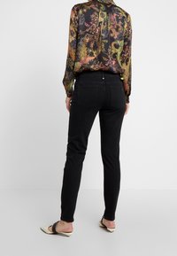 Svarta tajta jeans med en slät yta, tillsammans med en färgglad mönstrad blus. Jeansen har bakfickor och en medelhög midja.