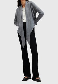 Szary kardigan z otwartym przodem wykonany z miękkiej dzianiny, o drapowanym fasonie zwężającym się z przodu, noszony na białej bluzce i czarnych spodniach.