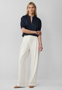 Blusa blu navy a maniche corte con scollo a V e maniche arricciate, abbinata a pantaloni larghi color crema e sandali chiari. Design semplice e moderno.