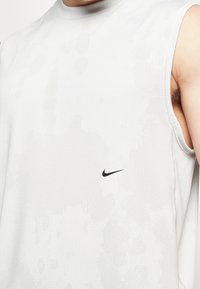 Débardeur blanc de sport avec un motif camouflage subtil et un petit logo Nike noir sur la poitrine, porté par une personne.