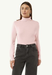 Helles rosa Rollkragensweatshirt mit langen Ärmeln, geripptem Kragen und glatter Textur, kombiniert mit hochgeschnittenen, dunkelgrauen Jeans mit Taschen.
