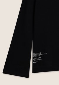 T-shirt nero a maniche lunghe in cotone, con testo stampato bianco sul bordo inferiore, dalla vestibilità rilassata e scollo standard.
