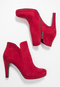 Rode suède enkellaarzen met hoge hak, voorzien van een ritssluiting aan de zijkant en een uitsnijding aan de buitenranden voor een moderne uitstraling.