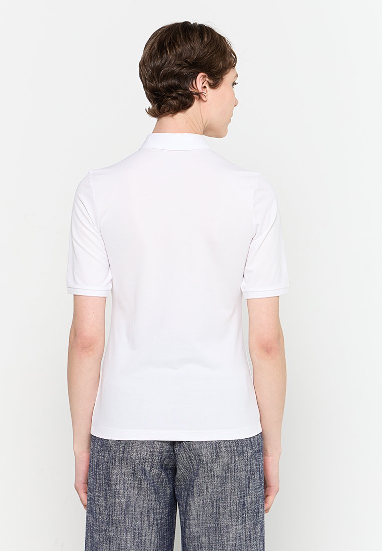 Weißes kurzärmliges Poloshirt mit Kragen, glatter Textur und taillierter Passform. Getragen mit blauen strukturierten Hosen.